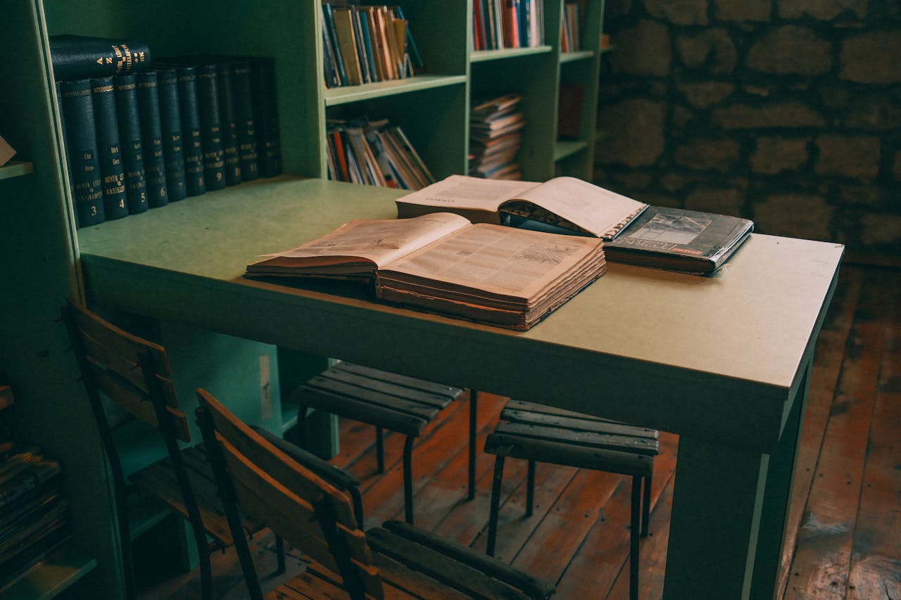 services-01 Warm-toned library interior featuring open books on a vintage table with green shelves.