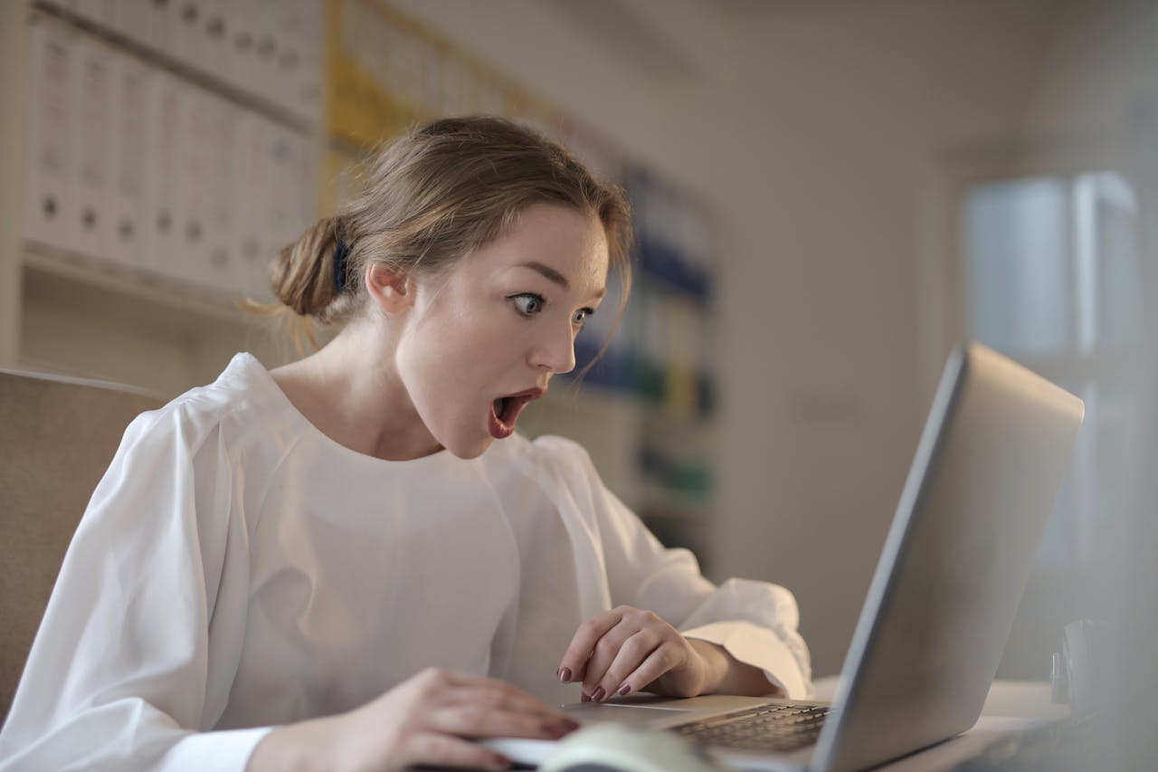 journey Surprised woman sitting at desk with laptop indoors, expressing amazement.